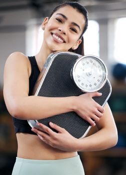 Lose weight, gain confidence. Portrait of a fit young woman holding a scale in a gym.