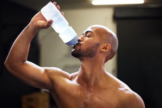 All your sweat, time and devotion will pay off. a muscular young man drinking water while exercising in a gym.