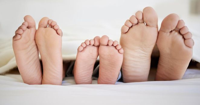 Being a family means you are a part of something. a family laying barefoot on a bed at home.