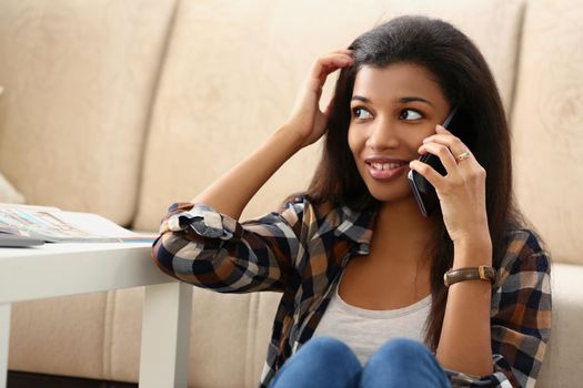 A dark-skinned girl on the floor house speaks on a phone