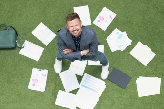 Businessman scattered documents on a green lawn, top view