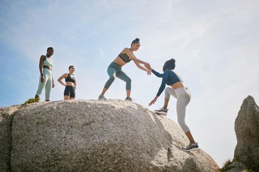 No one can do it alone. a woman helping her friend climb a boulder during a workout.