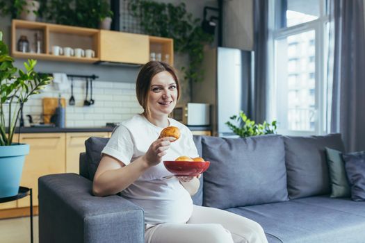 Pregnant woman at home sitting on sofa eating unhealthy and junk food donuts