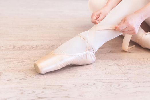 A seated ballerina tightens her pointe shoes