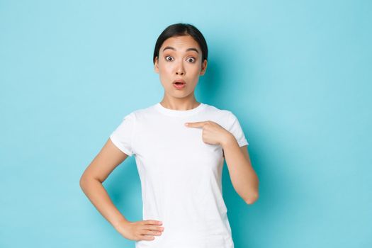 Surprised asian girl in white t-shirt pointing at herself with wondered unsure expression, being chosen or named, picked from the rest. Woman looking astonished winning something