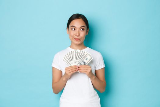 Shopping, money and finance concept. Thoughtful and creative pretty asian girl thinking where invest money, holding cash and looking upper right corner, making choice, deciding what buy