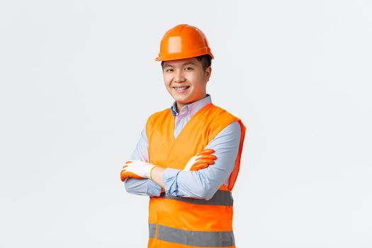 Building sector and industrial workers concept. Confident young asian engineer, construction manager in reflective clothes and helmet, cross arms and smiling sassy, ensuring quality, white background