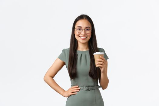 Smiling successful asian businesswoman in glasses standing confident, drinking morning coffee and starting new business day at office, manage own store from home, standing white background