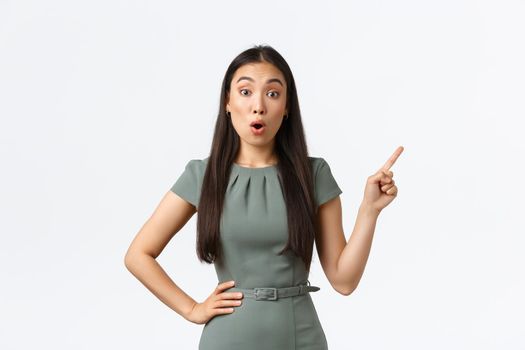 Small business owners, women entrepreneurs concept. Surprised and amazed asian businesswoman asking question about product, pointing finger upper right corner and look astounded