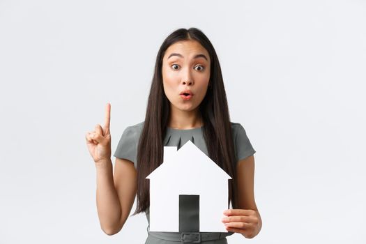 Insurance, loan, real estate and family concept. Thoughtful and creative asian woman have idea, found perfect home or apartment, raise index finger in eureka sign, holding paper house