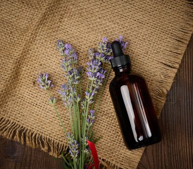 A glass brown bottle with a pipette and a bouquet of lavender on a brown wooden table. 