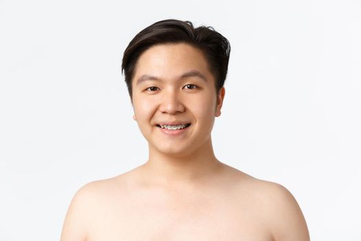 Beauty, skincare and hygiene concept. Close-up of smiling asian guy with braces standing naked over white background, advertisement of dermatology products, cleansers for acne prone skin