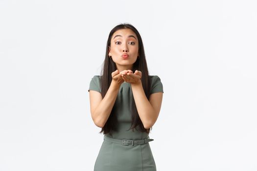 Small business owners, startup and work from home concept. Silly gorgeous asian woman in stylish dress pouting lips, sending air kiss at camera with coquettish expression, love her clients