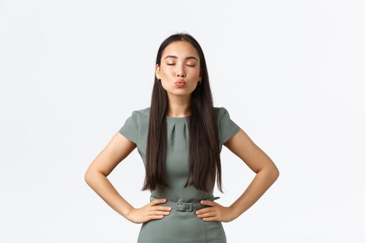 Small business owners, women entrepreneurs concept. Feminine gorgeous asian woman in stylish dress close eyes and pouting lips forward, waiting for kiss, standing white background