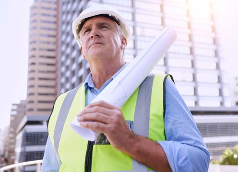 Hes ready to build something great. a handsome mature male construction worker carrying blueprints while standing outside.