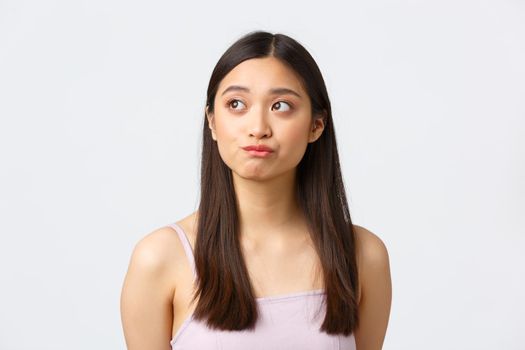 Concept of beauty, fashion and makeup products advertisement. Close-up portrait of beautiful indecisive asian girl having doubts, looking left and smirk unsure, hesitating over white background