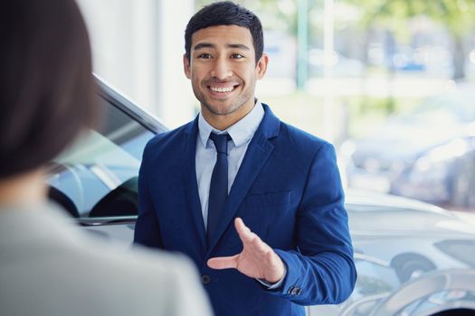 What can I do for you today. a handsome young male car salesman talking to a female customer on the showroom floor.