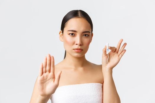 Beauty, personal and intimate care menstrual hygiene concept. Serious-looking beautiful asian girl in towel, showing stop gesture and tampon, encourage use menstrual cups or organic products