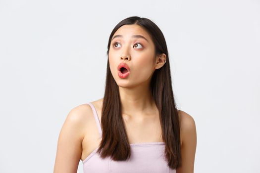 Beauty, fashion and people emotions concept. Impressed and amazed beautiful asian girl drop jaw, gasping and saying wow speechless, looking upper left corner excited, white background