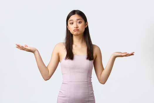 Luxury women, party and holidays concept. Clueless gloomy asian girl in evening dress, shrugging with hands spread sideways, dont know what product better, smirk unaware and doubtful