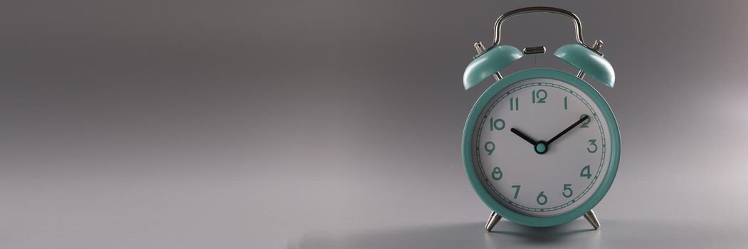 Turquoise alarm clock at ten o'clock on gray background