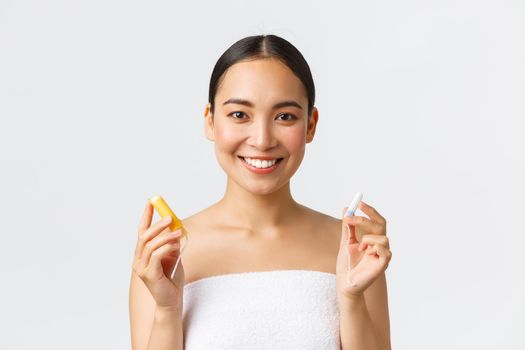 Beauty, personal and intimate care menstrual hygiene concept. Close-up of attractive asian girl in towel showing tampon with and without applicator, smiling at camera, white background