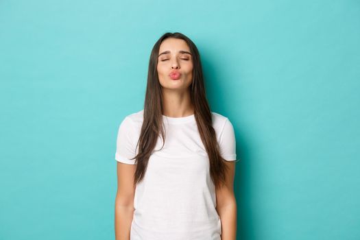 Portrait of cute girlfriend in white casual t-shirt, close eyes and pouting, waiting for kiss, standing over blue background