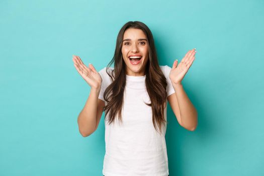 Image of excited attractive girl in white t-shirt, looking fascinated and clapping hands, applause from happiness, standing over blue background