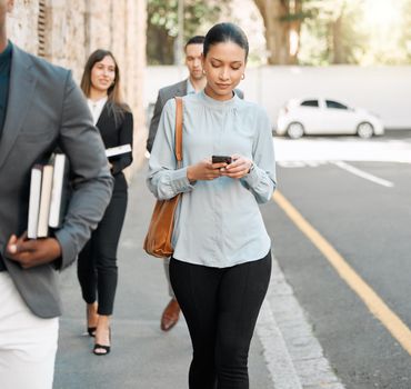 Email me those contracts. a businesswoman using her smartphone to send a text while walking.