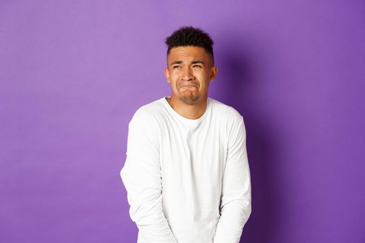 Image of silly guy waiting in line for toilet, grimacing and looking left, need to pee, standing over purple background