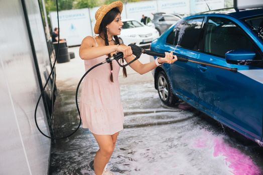 Brunette from a high-pressure hose washes the car