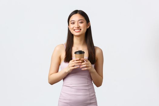 Lifestyle, people emotions and glamour concept. Beautiful young happy asian woman in dress, enjoying nice cup of coffee and smiling camera, order takeaway from cafe, white background