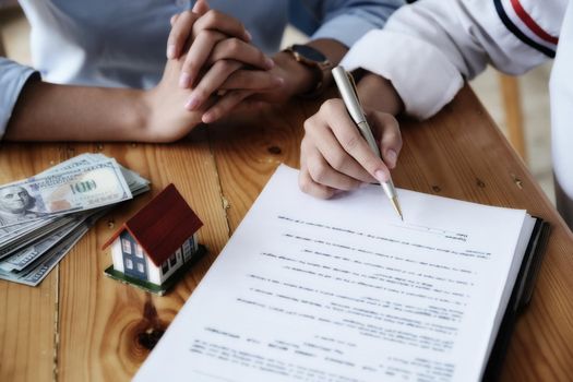 The customer holds a pen and reads the conditions in order to sign a house purchase contract with home insurance documents with the salesperson.
