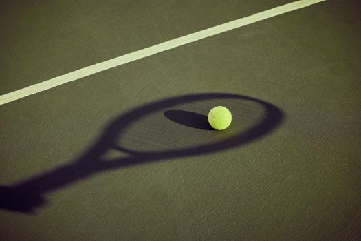 Ready to serve. a tennis ball lying on a court outlined by the shadow of a racket.