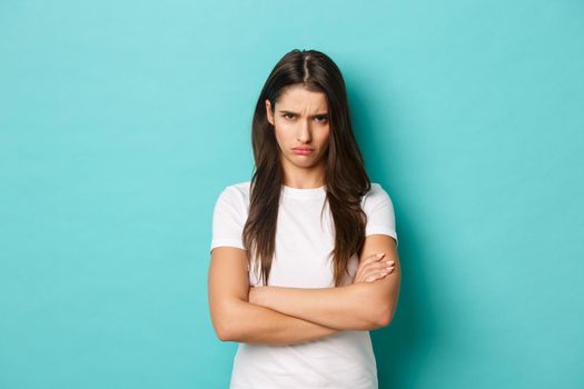 Image of upset sulking girl, feeling offended or jealous, cross arms chest and frowning angry, standing over blue background