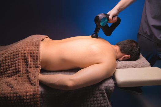 Physiotherapy of the upper back with a percussion massager. Therapist kneads the patient's upper back