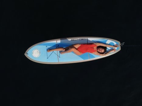 Aerial drone view on well looking middle aged woman with black hair in red swimsuit, swimming on sup in calm azure sea. Summer holiday vacation and travel concept.