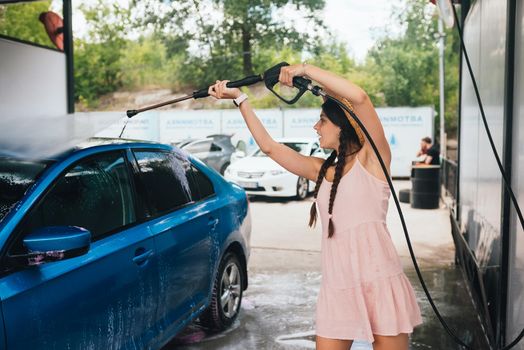 Brunette from a high-pressure hose washes the car