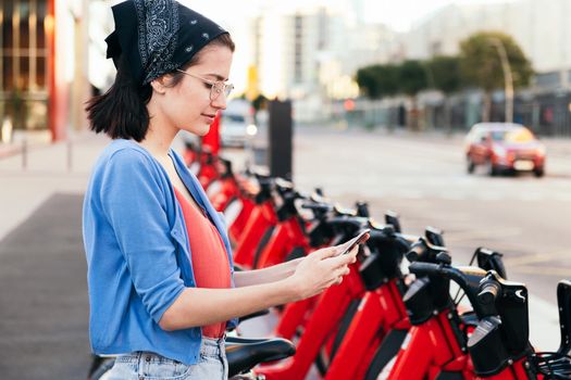 woman using phone next to a bike rental station