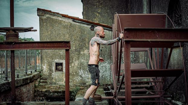 Frustrated man with tattooed body in an abandoned site old machinery