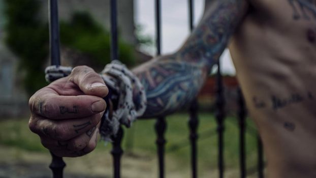 Details of tattooed hands of a man tied to grills behind him