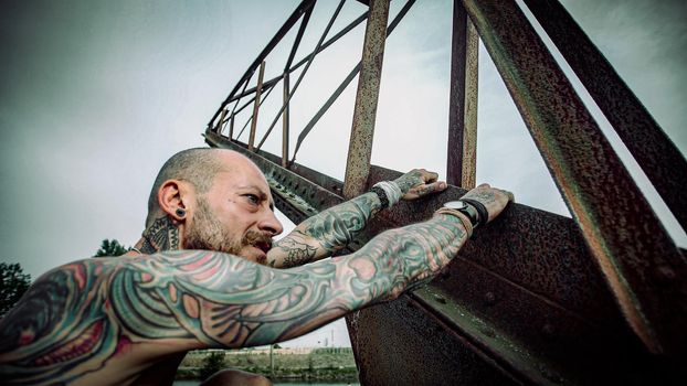 Man with tattooed body climbs on an old rustic crane and walks toward