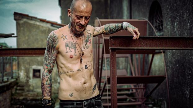 Frustrated man with tattooed body in an abandoned site old machinery