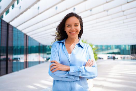 Confidence Businesswoman portrait with crossed hands. Pretty business woman 30 years old standing near office building dressed blue shirt.