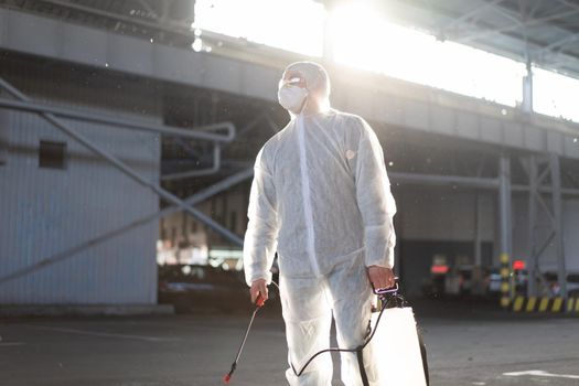 Man dressed white protective overalls spraying surface antibacterial sanitizer sprayer during quarantine