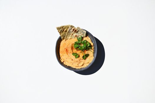 Chickpea hummus dip with pita bread on a blue ceramic bowl, above view on a white background with copy ad space for text