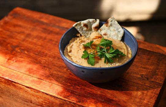 Chickpea hummus dip with pita bread on a blue ceramic bowl, above view on wooden background with copy ad space for text