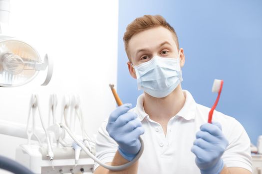 Professional male dentist holding a toothbrush and a drilling machine