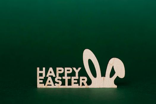 Wooden inscription Happy Easter and stylized bunny ears on a green background