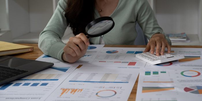 Tax inspector and financial auditor looking through magnifying glass, inspecting company financial papers, documents and reports
